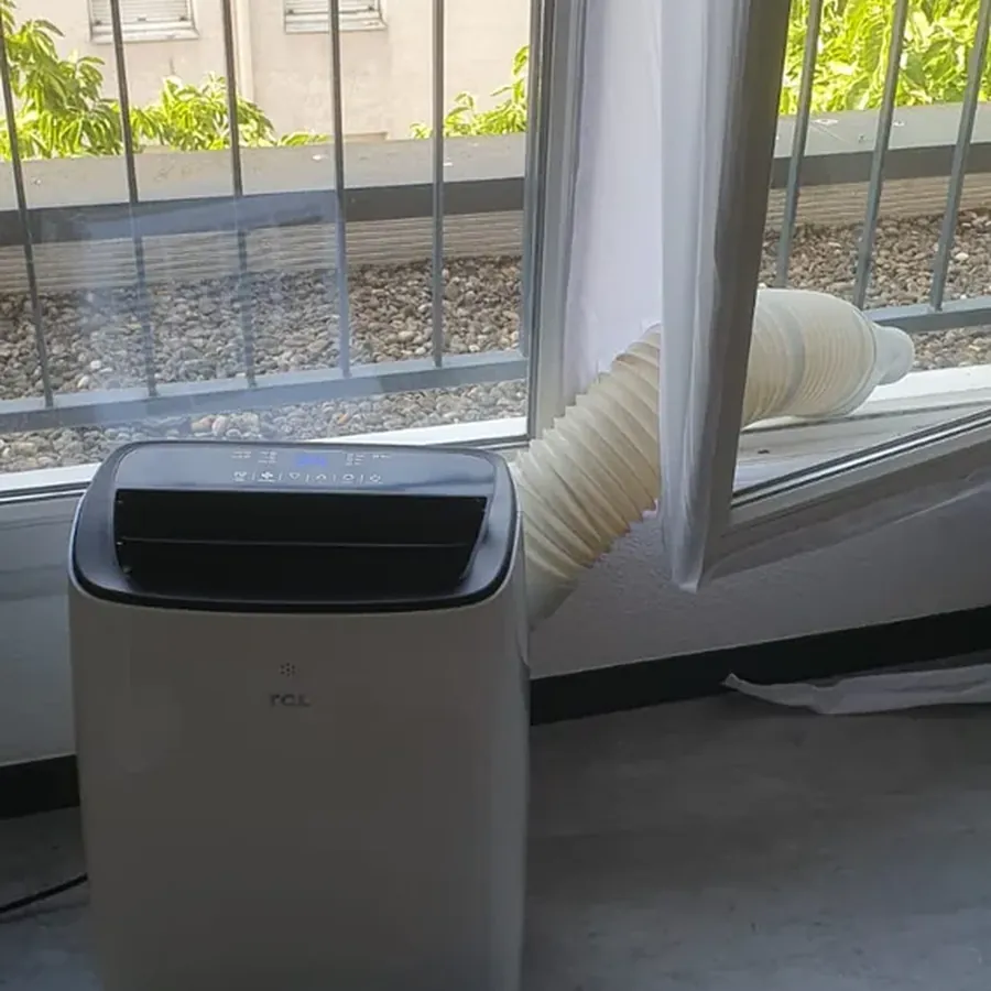 Climatiseur mobile installé devant une fenêtre, prêt à fonctionner