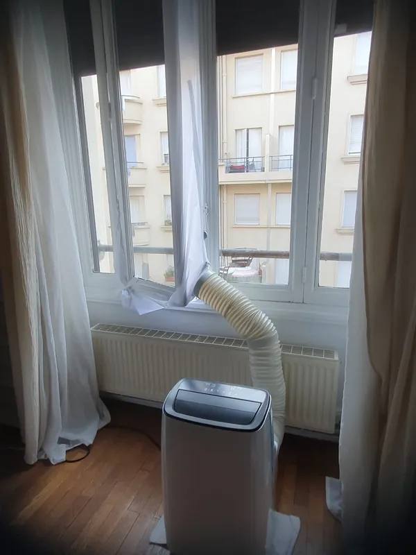 Climatiseur mobile installé près d'une fenêtre dans un séjour à Lyon, tuyau d'évacuation raccordé avec un kit de calfeutrage